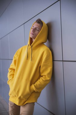 Sarı kapüşonlu ciddi bir genç, gri bir duvara karşı parlak elbiseli şık bir moda adamı.