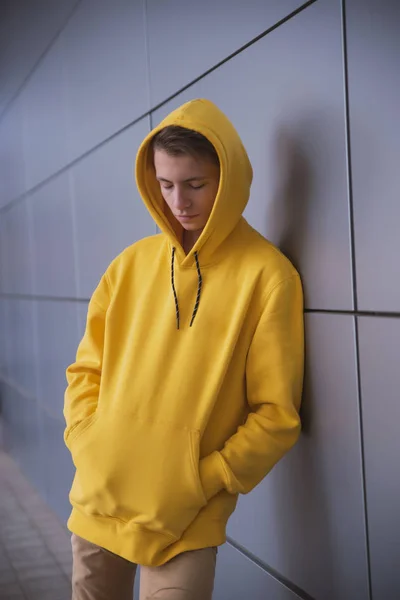 A serious young guy in a yellow hoodie, a cute stylish fashion man in bright clothes against a gray wall