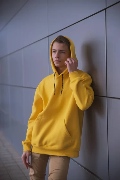 A serious young guy in a yellow hoodie, a cute stylish fashion man in bright clothes against a gray wall