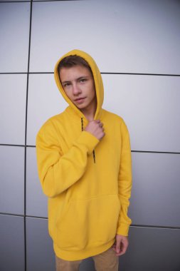 Sarı kapüşonlu ciddi bir genç, gri bir duvara karşı parlak elbiseli şık bir moda adamı.