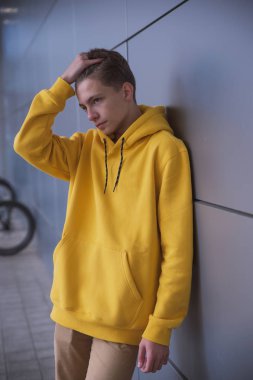 Sarı kapüşonlu ciddi bir genç, gri bir duvara karşı parlak elbiseli şık bir moda adamı.