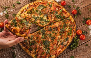 Elleri pizza için uzanır, kiraz domatesli ahşap bir masada uzanır.