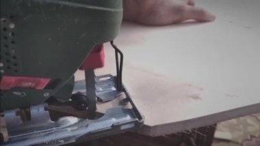 Elektrikli yapboz kontrplağı yavaş çekimde keser, uçan parçacıklarla odun keser, bir ülke arazisi üzerinde çalışır, kendi ellerinizle bir ev inşa edersiniz.