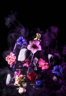 Cam bir parfüm şişesi kırılır ve parlak bahar çiçekleri ve mavi ve mor buhar bulutları koyu bir arka plana doğru fışkırır.