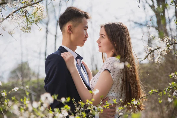 Asian guy with a girl of European origin hugging in a blooming garden