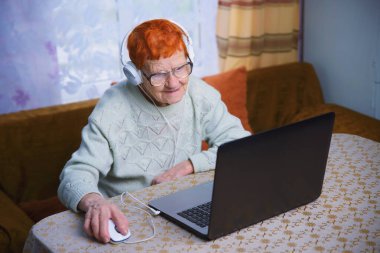 Yaşlı bir kadın dizüstü bilgisayarda çalışıyor, bir büyükanne mobil iletişim ve internet teknolojilerinde ustalaşıyor ve yaşlılar sevdikleriyle kendi kendilerini izole etme koşullarında iletişim kurmak için aletler kullanıyorlar.