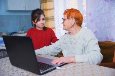 Bir torun büyükannesine bilgisayarda çalışmayı öğretir, küçük bir kız yaşlı bir kadınla dizüstü bilgisayarda oynar, internet teknolojileri çalışmasında yaşlılara bakar.
