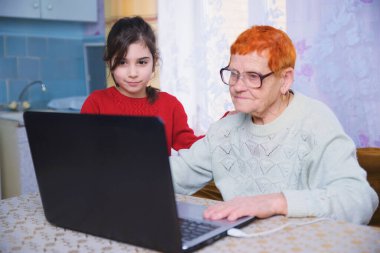 Bir torun büyükannesine bilgisayarda çalışmayı öğretir, küçük bir kız yaşlı bir kadınla dizüstü bilgisayarda oynar, internet teknolojileri çalışmasında yaşlılara bakar.
