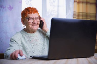 Yaşlı bir kadın dizüstü bilgisayarda çalışıyor, bir büyükanne mobil iletişim ve internet teknolojilerinde ustalaşıyor ve yaşlılar sevdikleriyle kendi kendilerini izole etme koşullarında iletişim kurmak için aletler kullanıyorlar.