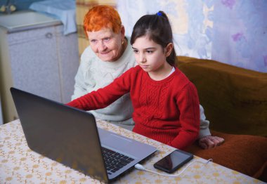 Bir torun büyükannesine bilgisayarda çalışmayı öğretir, küçük bir kız yaşlı bir kadınla dizüstü bilgisayarda oynar, internet teknolojileri çalışmasında yaşlılara bakar.