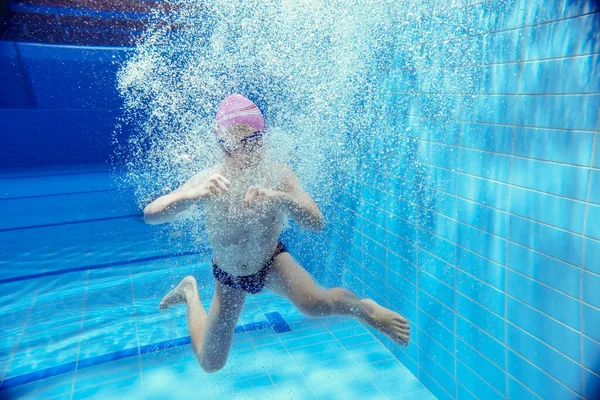 プールの水の下で泳ぐ少年キャップとガラスの中で陽気で感情的な子供水の下で潜る — ストック写真