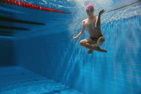プールの水の下で泳ぐ少年キャップとガラスの中で陽気で感情的な子供水の下で潜る — ストック写真