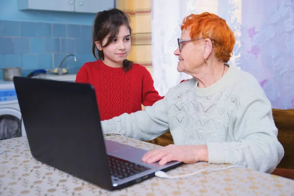 A granddaughter teaches her grandmother to work on a computer, a little girl plays on a laptop with an elderly woman, taking care of the elderly in the study of Internet technologies