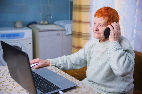 An elderly woman is working on a laptop, a grandmother is mastering mobile communication and Internet technologies, and elderly people use gadgets to communicate with their loved ones in conditions of self-isolation