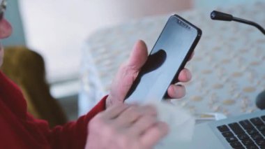 Yaşlı bir kadın evde dizüstü bilgisayar ve akıllı telefona antiseptik, temizlik ve koronavirüs önleme ilacı veriyor. Cihazların üzerinde mikro organizmalarla savaşmak