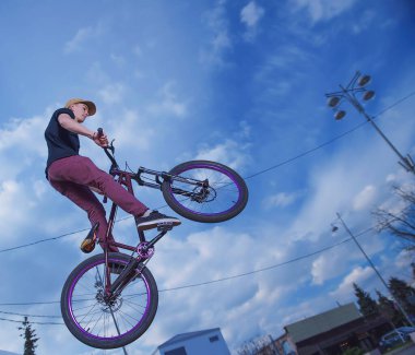 Bisikletli bir adam gökyüzüne doğru sıçrıyor. Alt açıdan bisikletle atlama sahnesi var. MTB motosikletli bir bisikletçi güzel mavi gökyüzüne karşı bir numara yapar.