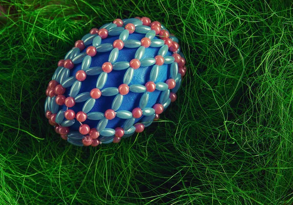 Easter eggs in beads on a green and wooden background. The symbol of the Easter holiday is covered with beads. Bright Easter eggs in a basket