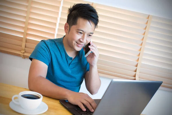 Hombre joven trabajando en el ordenador portátil y hablando en el teléfono móvil . — Foto de Stock