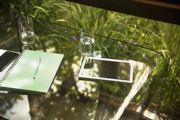 Tablette numérique et verres d'eau sur table en verre — Photo de stock