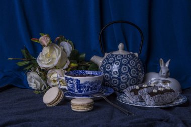 Natürmort mavi tonlarda gül, çay ve tatlılar