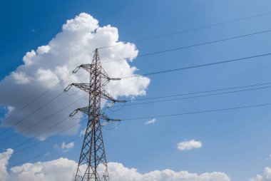 Elektrik iletim hatları (yüksek voltaj kulesi) yüksek voltaj hatları. Elektrik transferi, tarımsal bölgelerden geçerek destekleniyor. Güneşli bir gün ve mavi gökyüzünde sirus bulutları var.