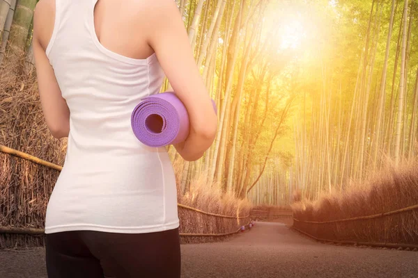 Joven asiática mujer sosteniendo su yoga mat en naturaleza bambú bosque . — Foto de Stock