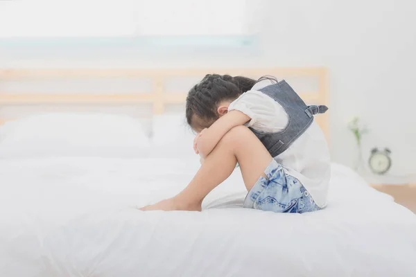 Depressziós ázsiai kislány ül az ágyon, átölelve a térdére a szomorú moody. — Stock Fotó