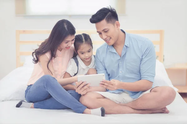 Boldog család, a hálószobában, ázsiai apa és anya rajzfilm a smart tábla lányával együtt nézni otthon. — Stock Fotó