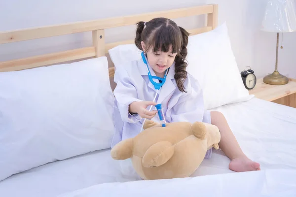 Χαριτωμένο μικρό ασιατικό κορίτσι απολαύσετε παίζοντας τον γιατρό με σύνολο παιχνιδιών ο γιατρός και χαριτωμένο κούκλα στο σπίτι. — Φωτογραφία Αρχείου