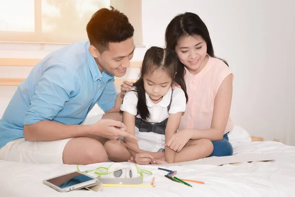 Glückliche Familie im Schlafzimmer, asiatischer Vater und Mutter, die ihrer Tochter das Lernen zu Hause beibringt. — Stockfoto