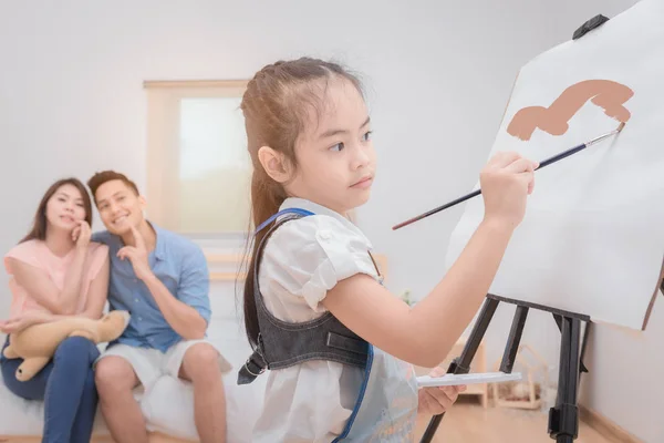 Asiático padre y madre buscando hija niño pintura con acuarela en el caballete en casa —  Fotos de Stock