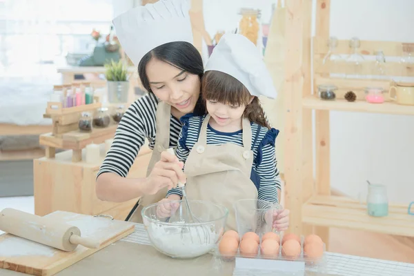 Asian mother and her daughter are preparing the dough to make a cake in the kitchen room on vacation