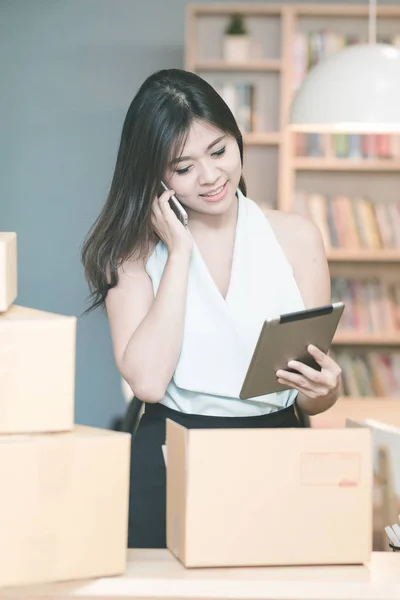 Joven emprendedora comprobando el stock de productos en la tableta inteligente mientras habla con su cliente en la oficina en casa —  Fotos de Stock