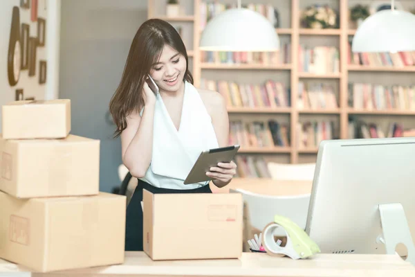 Jovem empreendedora verificando o estoque de produtos no tablet inteligente enquanto conversa com seu cliente no escritório em casa — Fotografia de Stock