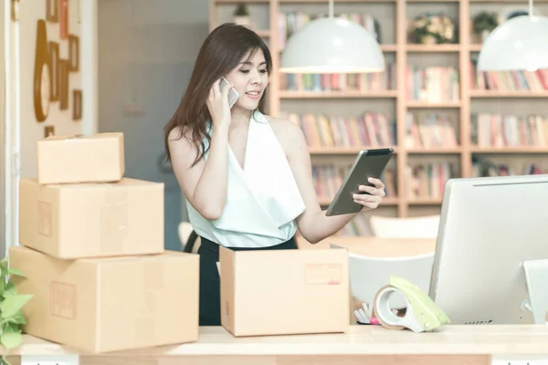 Ung entreprenør som sjekker produkter på smarttabletten mens hun snakker med kunden på hjemmekontoret – stockfoto