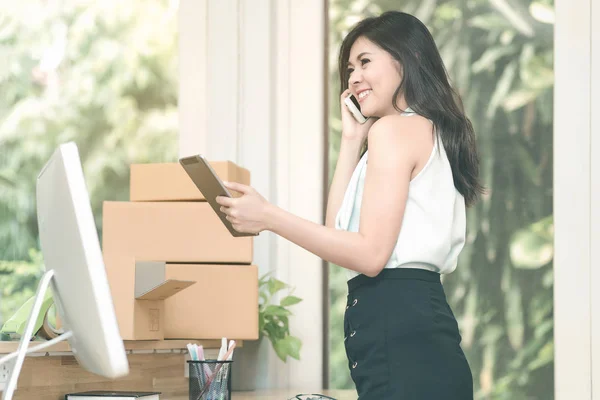 Young entrepreneur checking products stock on the smart tablet while talking to her customer at home office — Stock Photo, Image