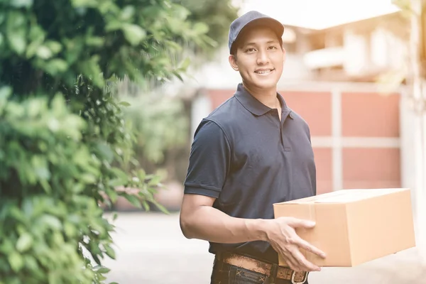 Knappe jonge Aziatische levering man die lacht terwijl een kartonnen doos levering aan zijn klant. — Stockfoto