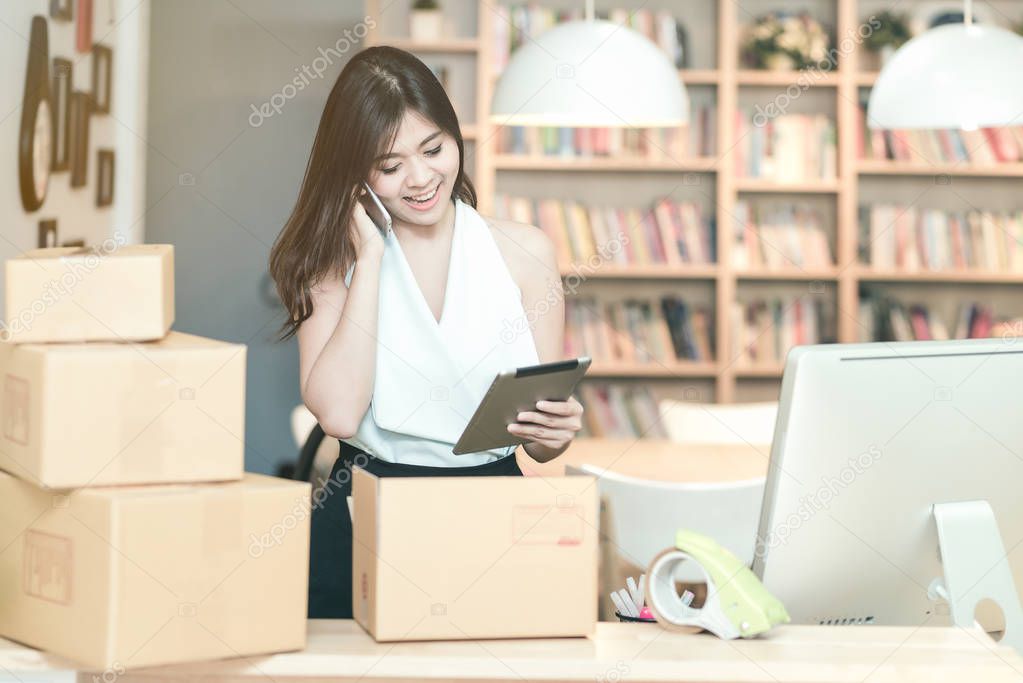 Young entrepreneur checking products stock on the smart tablet while talking to her customer at home office