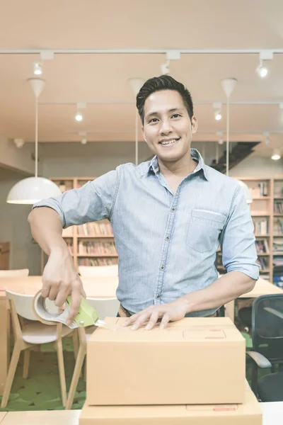 Young asian entrepreneur packing product into the box for his customers after received order at home office — Stock Photo, Image