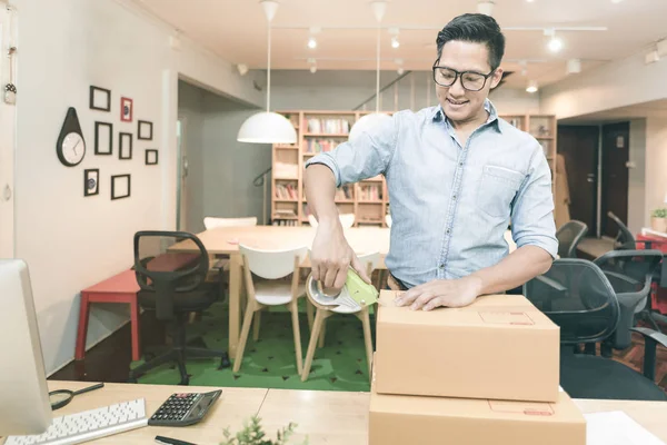 Young asian entrepreneur packing product into the box for his customers after received order at home office. — Stock Photo, Image