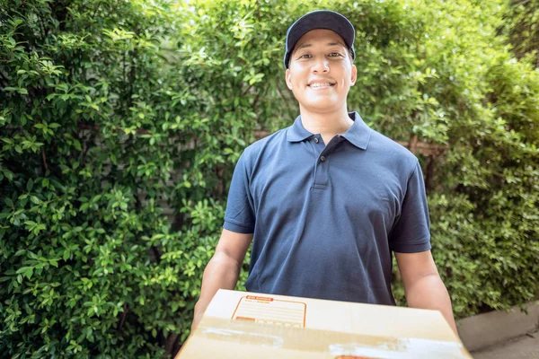 Hermoso joven asiático repartidor hombre sonriendo mientras sostiene una caja de cartón entrega a su cliente . —  Fotos de Stock