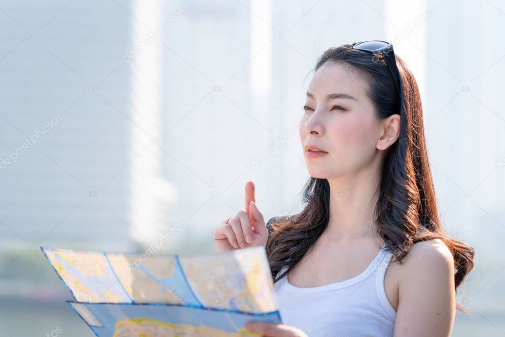 Beautiful asian tourist woman looking at map for searching location of landmark.