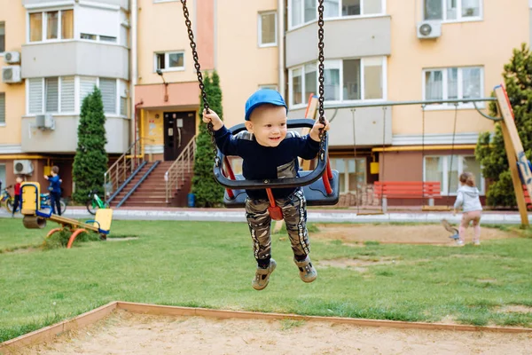 Engraçado e bonito menino se alegra, passeios em um balanço de crianças, joga no parque infantil — Fotografia de Stock