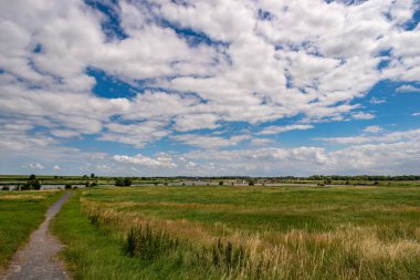 Arka planda Marina 'nın olduğu bir lağım manzarası ve mavi gökyüzünde muhteşem beyaz bulutlar, Greetsiel, Aşağı Saksonya, Kuzey Almanya 