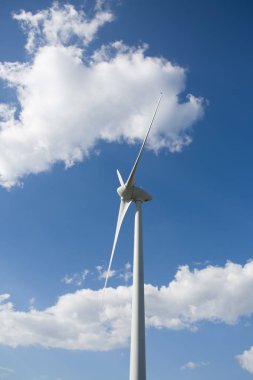 Dağların tepesinde bir rüzgar türbini, arka planda mavi gökyüzü