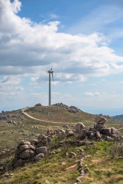 Dağların tepesinde bir rüzgar türbini, arka planda mavi gökyüzü