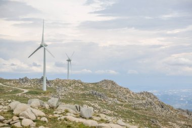 Dağların tepesindeki rüzgar türbinlerinin görüntüsü, arkaplan olarak bulutlu gökyüzü