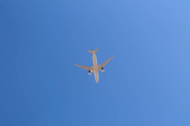 Uçan bir ticari uçağın alt görüntüsü, arka plan olarak mavi gökyüzü.