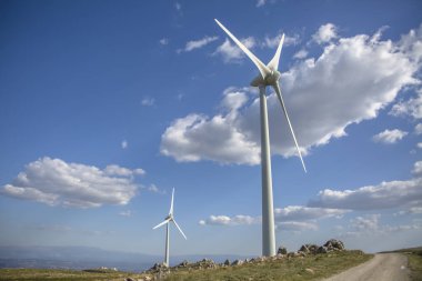 Dağların tepesindeki rüzgar türbinlerinin görüntüsü, arkaplan olarak bulutlu gökyüzü