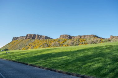 Holyrood Parkı 'ndaki Salisbury kayalıklarının manzarası. Yeşil alanlar, yürüyen ve arayan turistler, Edinburgh' da mavi gökyüzü.